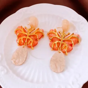 Vintage butterfly drop earrings with orange resin wings and gold plating on a ceramic tray