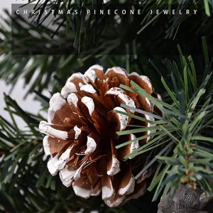 Christmas pinecone ornament with snow-tipped scales on a green pine needle background