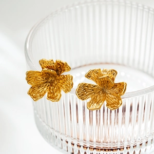 Detailed close-up of 18K gold plated flower earring on a clear textured glass edge