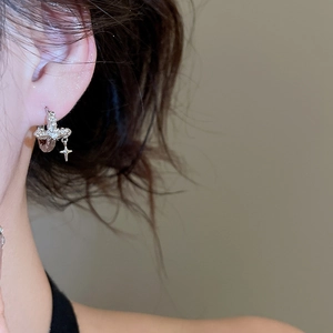 Close-up of silver earrings featuring a sparkling zircon cross pendant worn by a model