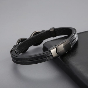 Close-up of black braided leather men's bracelet with dark metal clasp on leather background