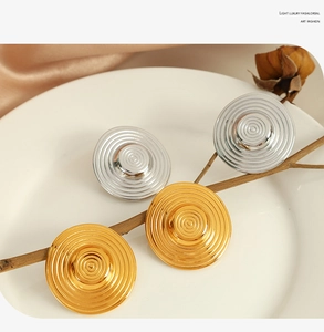 Detailed close-up of gold and silver textured hoop earrings on a ceramic dish with branches