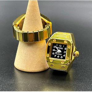 Detail view of gold finger watch showing square black dial and flexible link band