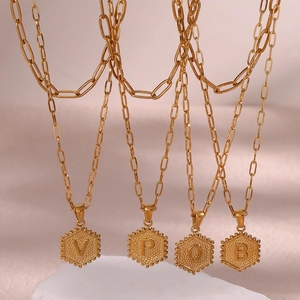 Detailed macro view of gold-tone paperclip chains with textured hexagonal initial pendants