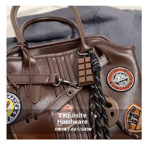 Detail einer braunen Leder-Schultertasche mit Stick-Patches und Schokoladen-Anhänger
