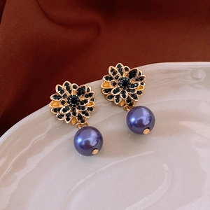 Detail of flower earrings featuring black crystals, gold finish, and a purple pearl drop