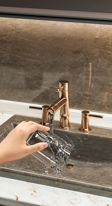 Three-hole split faucet in rose gold finish on marble countertop with water flow