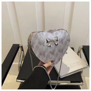 Detail of silver heart-shaped shoulder bag with metal bow and chain strap being held