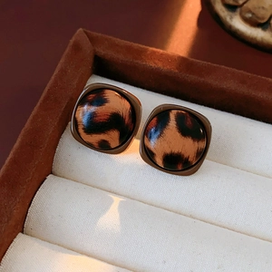 Gros plan de boucles d'oreilles carrées imprimé léopard en similicuir dans une boîte vintage