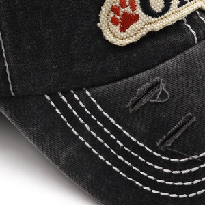 Detail of washed black cotton baseball cap showing white stitching and distressed torn brim