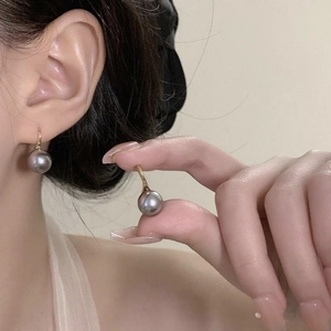 Detail view of a 18K gold hook earring with a premium grey pearl on a soft background