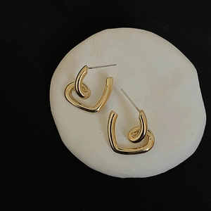 Detailed view of twisted gold-plated heart earrings on a white stone pedestal