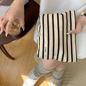 Detail of black and white striped canvas toiletry bag held by a model in a cozy cafe setting