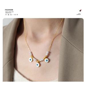 Detail of gold evil eye necklace with pearls on a model wearing a brown blazer