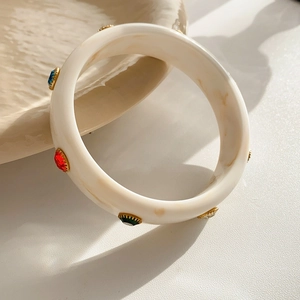 Detail of acrylic bangle with marble pattern and colorful gemstones in gold setting