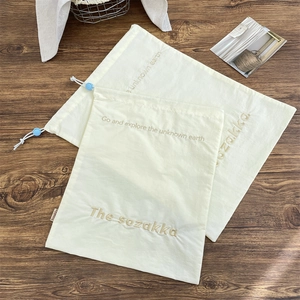 Detail of cream drawstring bags with blue toggles and embroidery on wooden background
