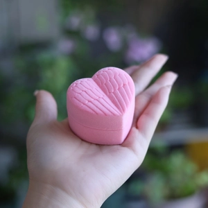 Pink heart-shaped velvet jewelry box with angel wing relief held in hand showing size