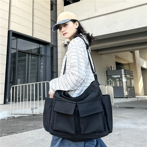 Black canvas messenger bag with large pockets shown on model in outdoor setting