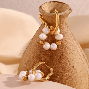 Détail macro de boucles d'oreilles dorées en U avec cinq perles blanches et billes dorées