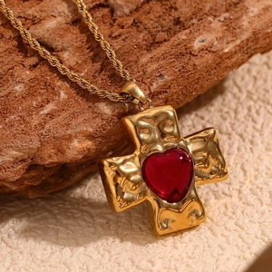 Close-up of a 18K gold plated cross pendant with a red heart gem on a textured twist chain