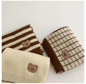Close-up of knitted children's scarves with bear patches in cream and coffee tones