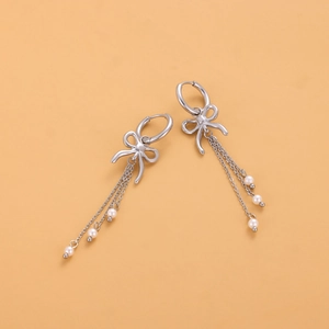 Détail de boucles d'oreilles nœud argentées avec de longs pompons et des perles blanches