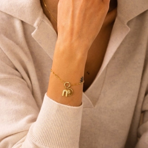 Gold chain bracelet with rainbow and floral charm pendants worn on a beige sweater