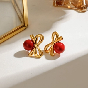 Boucles d'oreilles nœuds dorés élégantes avec perles rouges sur fond épuré