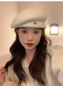 Detail of cream wool beret with gold metal M letter badge worn by a model