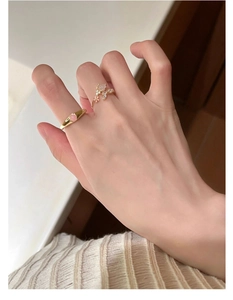 Detailed view of two gold floral rings with pink gemstones worn on a white knit sweater