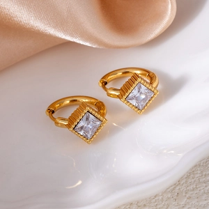 Detailed view of square gold earrings with clear crystals on a white textured tray