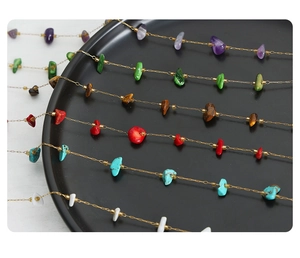 Macro view of colorful natural stone beads and gold chain on minimalist tray