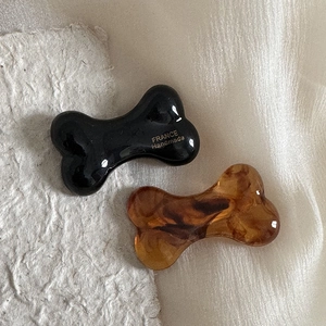 Cute bone-shaped hair clips in black and tortoiseshell finish on textured background