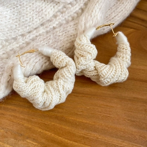 Dettaglio di orecchini a cerchio in maglia avorio con ganci dorati su legno