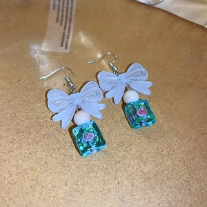 Macro detail of geometric drop earrings with ribbon bow and resin flower cube