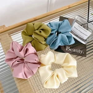 Set of 4 elegant satin scrunchies in pink, green, blue, and cream white on glass