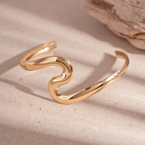 Minimalist wavy gold metal open bangle bracelet displayed on a natural stone background