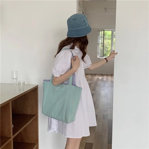 Bolso tote de lona a cuadros azules y verdes llevado por una modelo en estilo minimalista