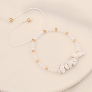 Detail of handmade beaded bracelet with white matte stones and gold accents on woven cord