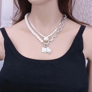 Close-up of layered snake chain necklace with baroque pearl and engraved square pendant
