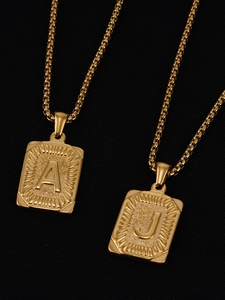 Detalle de colgantes cuadrados bañados en oro de 18K con grabados A y J en cadenas box