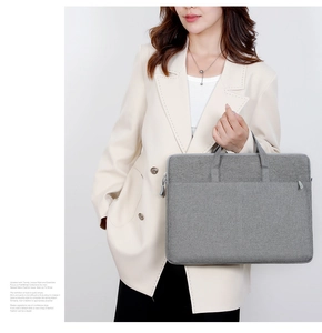 Graue Laptoptasche aus Stoff handgehalten, zeigt Textur und Details der Reißverschlusstasche