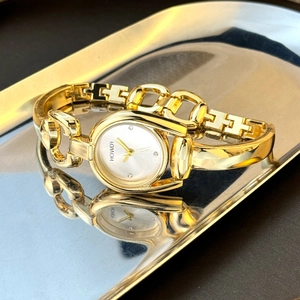 Detail of a horseshoe-shaped gold women's watch with a sleek polished metal bracelet