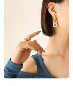 Macro shot of stylish gold letter B earring paired with minimalist textured gold rings