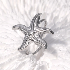 Silver starfish open ring in stainless steel with hammered texture on white coral background