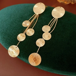 Detailed shot of gold fringe drop earrings with textured round metal discs on velvet