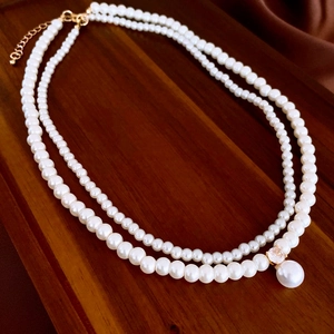 Double-layered pearl necklace with zircon pendant and gold chain on silk background