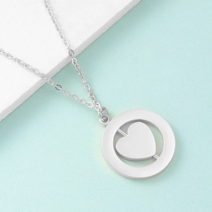 Detail of silver spinning heart pendant necklace on white stone with light blue background