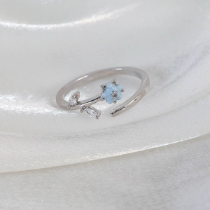 Macro shot of light blue enamel flower ring with marquise zircons on silk background