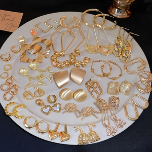 Flat lay of diverse golden geometric earrings on a ceramic dish over a black background